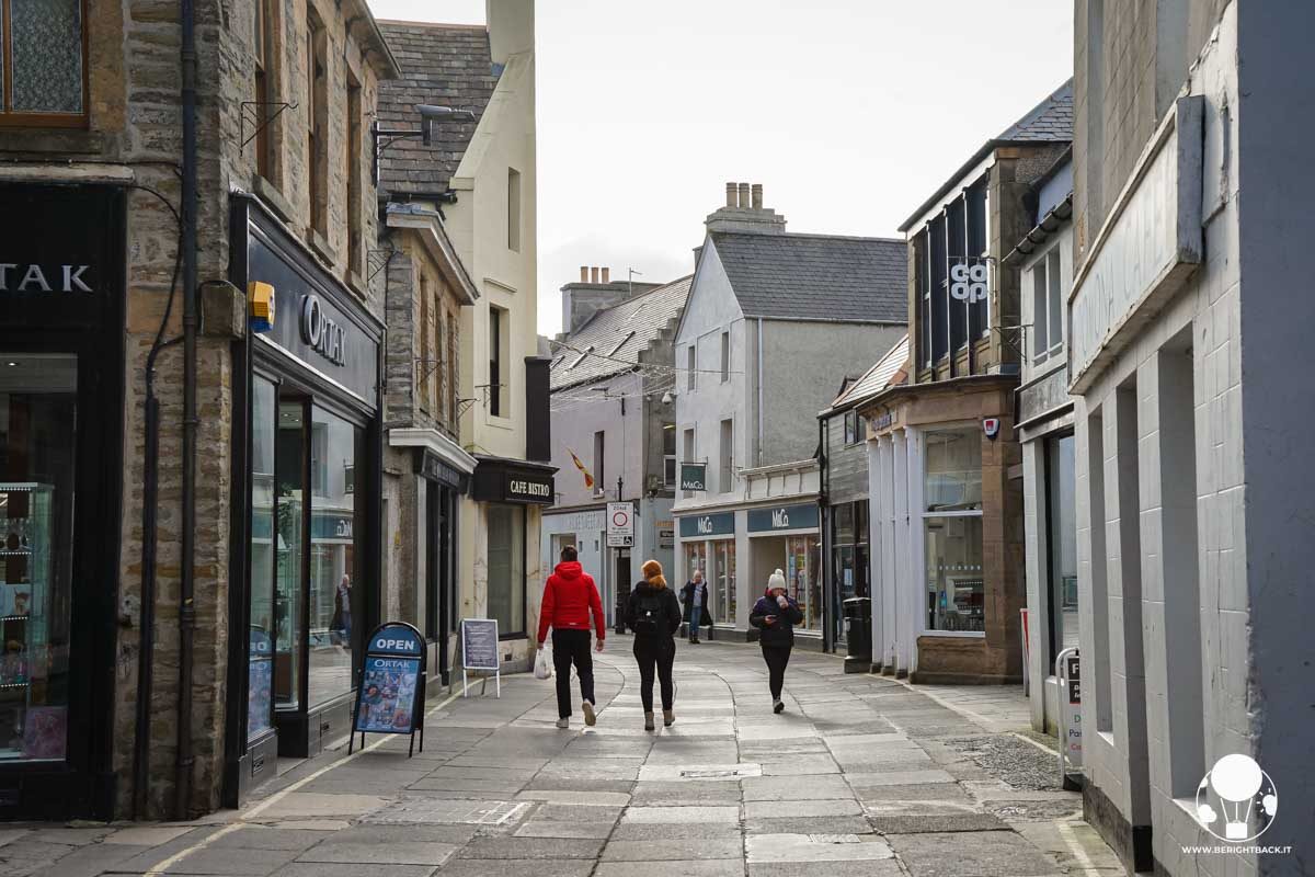 strada lastricata con poche persone che camminano e negozi che vi si affacciano