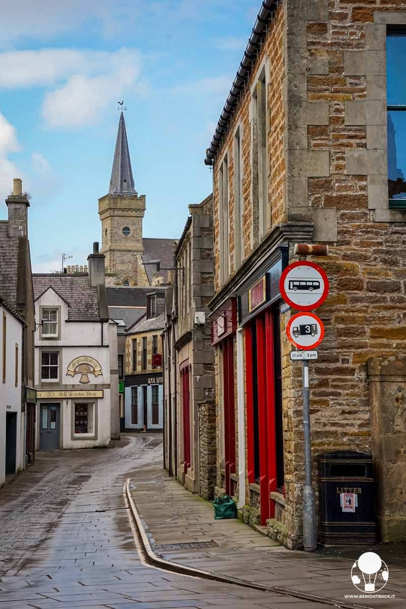 vicolo su cui si affacciano negozi e con un campanile sullo sfondo